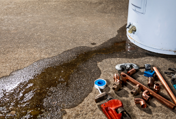 Water leaks from a water heater onto a concrete floor with tools lying on the ground beside.